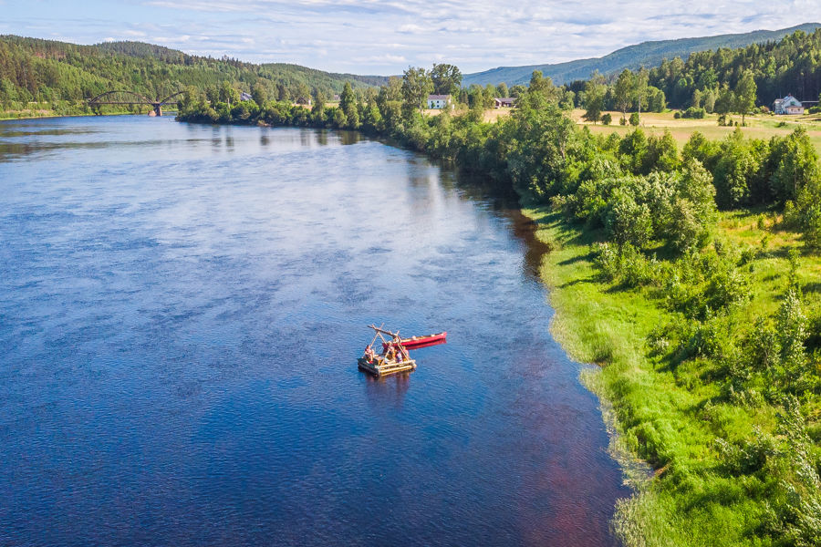 En flotte med en kanot på en älv, omgiven av grönskande värmländsk natur.